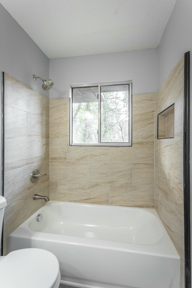 bathroom featuring a textured ceiling, tiled shower / bath combo, and toilet