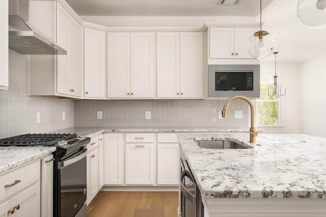 kitchen with tasteful backsplash, gas range oven, light wood-type flooring, wall chimney range hood, and a sink