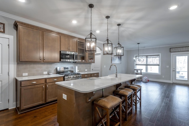 kitchen with pendant lighting, backsplash, stainless steel appliances, crown molding, and a center island with sink