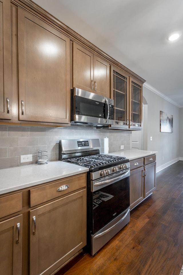 kitchen featuring crown molding, dark hardwood / wood-style floors, decorative backsplash, and appliances with stainless steel finishes