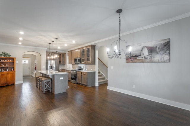 kitchen with appliances with stainless steel finishes, dark hardwood / wood-style floors, pendant lighting, a kitchen bar, and a center island with sink