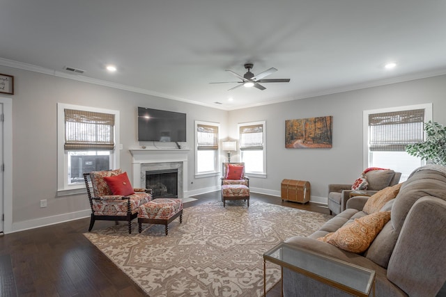 living room with a high end fireplace, dark wood-type flooring, ornamental molding, and ceiling fan