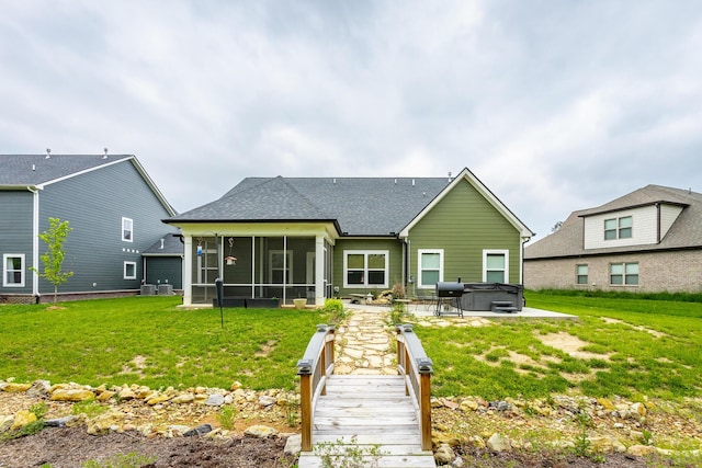 back of house featuring a sunroom, a yard, a shingled roof, and a hot tub