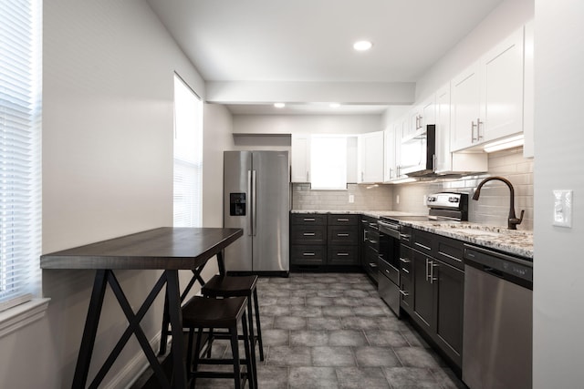 kitchen featuring sink, white cabinetry, stainless steel appliances, light stone countertops, and decorative backsplash