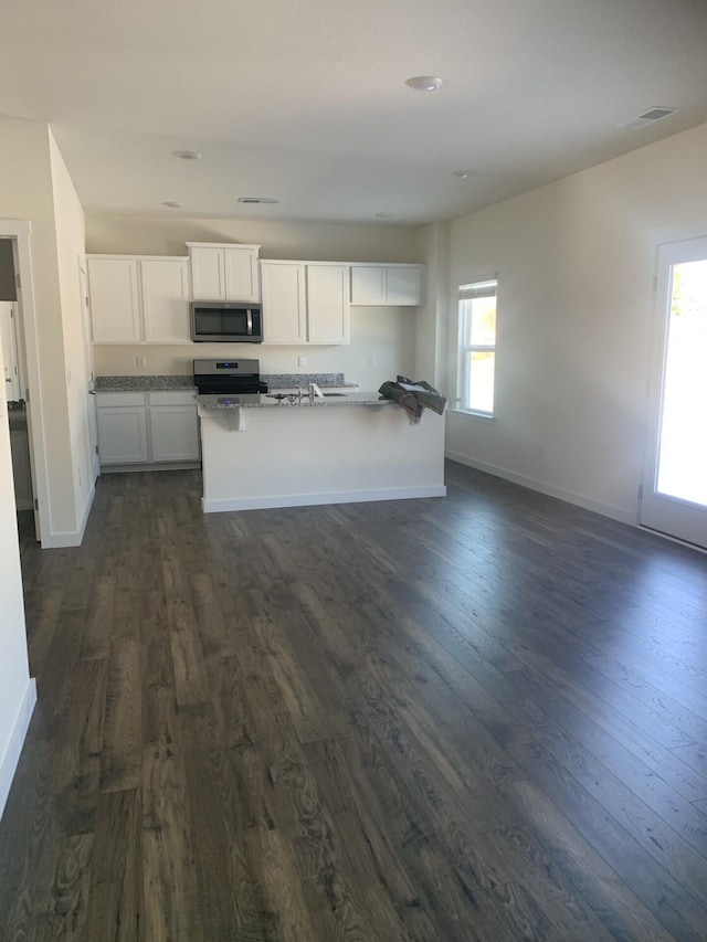 kitchen with appliances with stainless steel finishes, dark hardwood / wood-style floors, a kitchen island with sink, and white cabinets