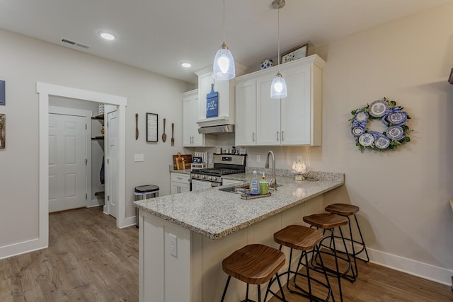 kitchen featuring a breakfast bar, white cabinetry, light stone counters, hanging light fixtures, and stainless steel range with gas cooktop