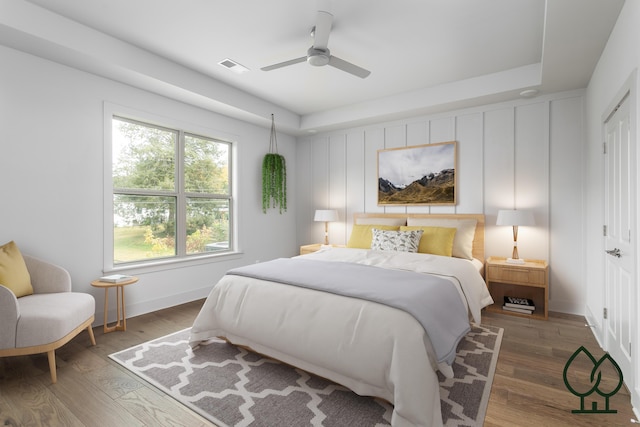 bedroom with a tray ceiling, dark hardwood / wood-style floors, and ceiling fan