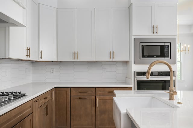 kitchen with sink, white cabinetry, custom range hood, stainless steel appliances, and backsplash