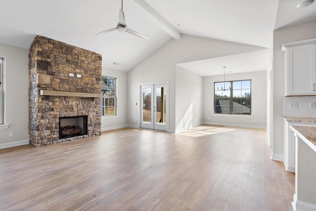 unfurnished living room with ceiling fan, beam ceiling, high vaulted ceiling, a stone fireplace, and light wood-type flooring