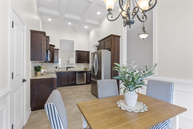 dining area featuring a towering ceiling, sink, beam ceiling, coffered ceiling, and an inviting chandelier