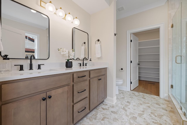 bathroom with a shower with door, vanity, crown molding, and toilet