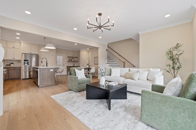 living room featuring crown molding, a chandelier, sink, and light hardwood / wood-style flooring