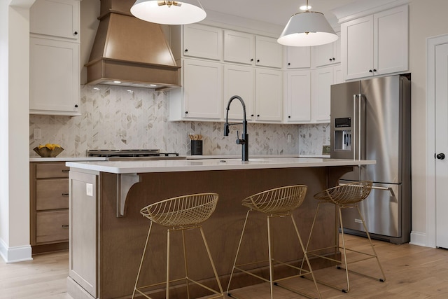 kitchen featuring high end fridge, custom exhaust hood, an island with sink, and a kitchen bar