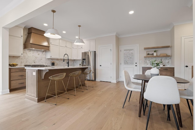 kitchen with premium range hood, high end fridge, an island with sink, pendant lighting, and decorative backsplash