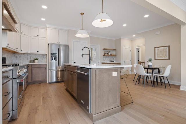 kitchen with a breakfast bar, a kitchen island with sink, high end appliances, white cabinets, and decorative light fixtures