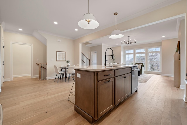 kitchen with pendant lighting, light hardwood / wood-style floors, sink, and a center island with sink