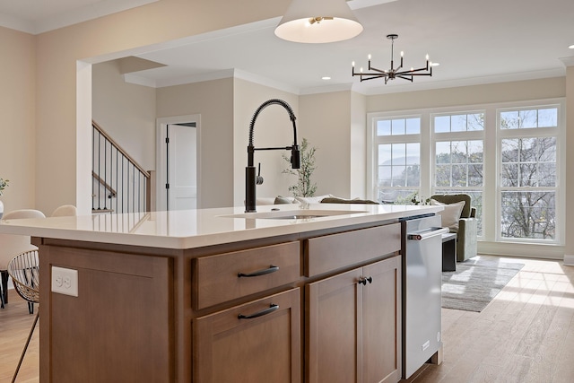 kitchen featuring sink, hanging light fixtures, ornamental molding, light hardwood / wood-style floors, and a center island with sink