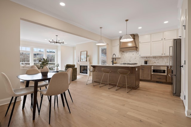 kitchen with decorative light fixtures, an island with sink, white cabinetry, decorative backsplash, and custom exhaust hood