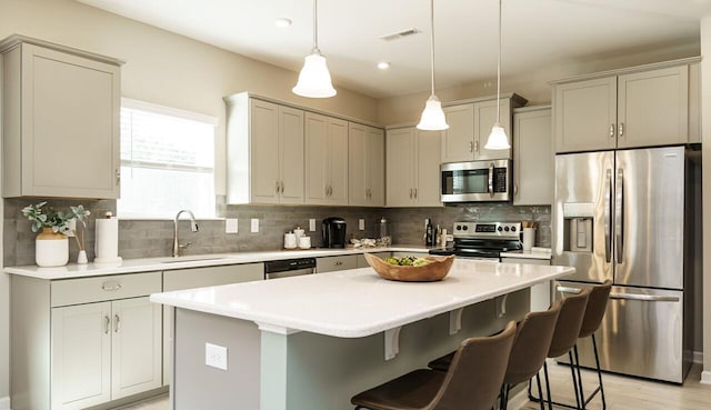 kitchen with a kitchen bar, sink, a kitchen island, pendant lighting, and stainless steel appliances