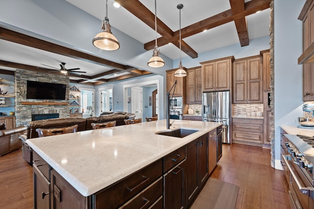 kitchen with appliances with stainless steel finishes, a fireplace, sink, dark hardwood / wood-style flooring, and a kitchen island with sink