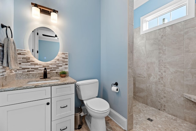 bathroom with vanity, toilet, a tile shower, and backsplash