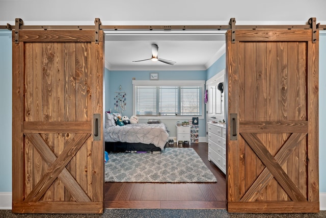 bedroom with ceiling fan, ornamental molding, a barn door, and dark hardwood / wood-style flooring