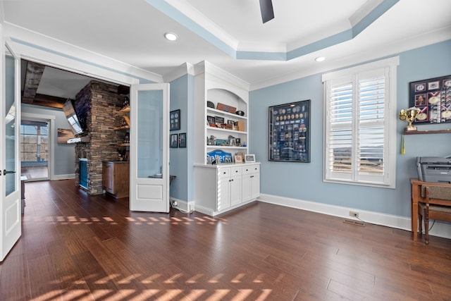 interior space with built in shelves, dark hardwood / wood-style floors, a stone fireplace, and a tray ceiling