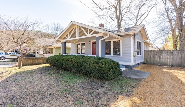 view of front of house featuring covered porch, fence, and a chimney