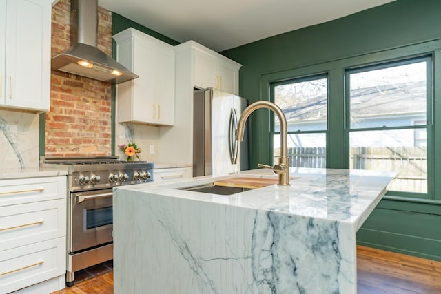 kitchen featuring white cabinetry, light stone counters, stainless steel appliances, plenty of natural light, and wall chimney range hood