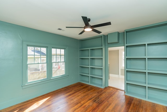 unfurnished room with dark wood-type flooring, built in features, and ceiling fan