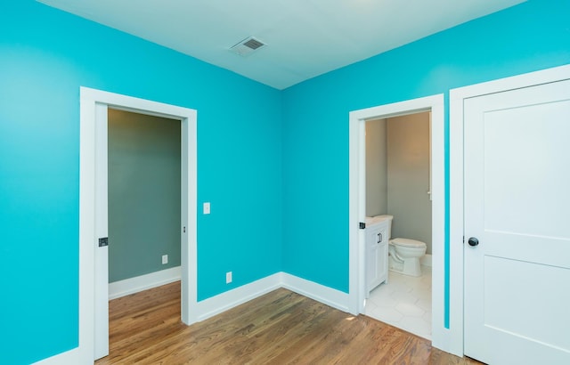 unfurnished bedroom featuring hardwood / wood-style floors and ensuite bath