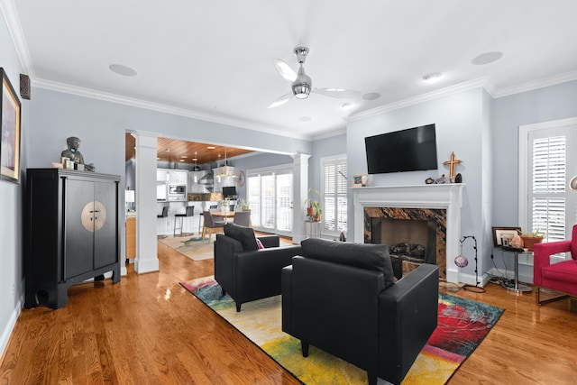 living room featuring decorative columns, wood-type flooring, ornamental molding, and a fireplace