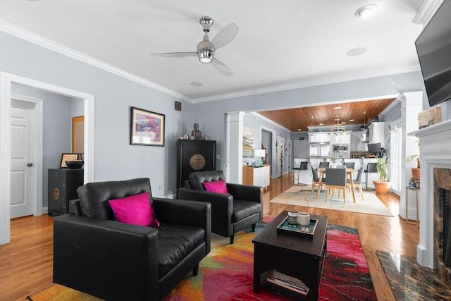 living room featuring crown molding, ceiling fan, decorative columns, a fireplace, and light hardwood / wood-style floors