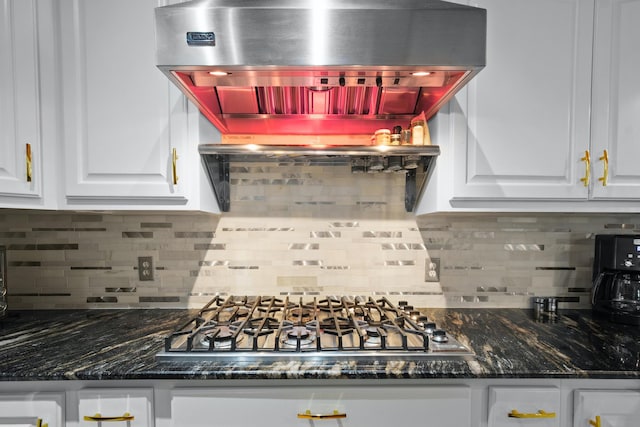 kitchen with dark stone countertops, island range hood, stainless steel gas stovetop, and white cabinets