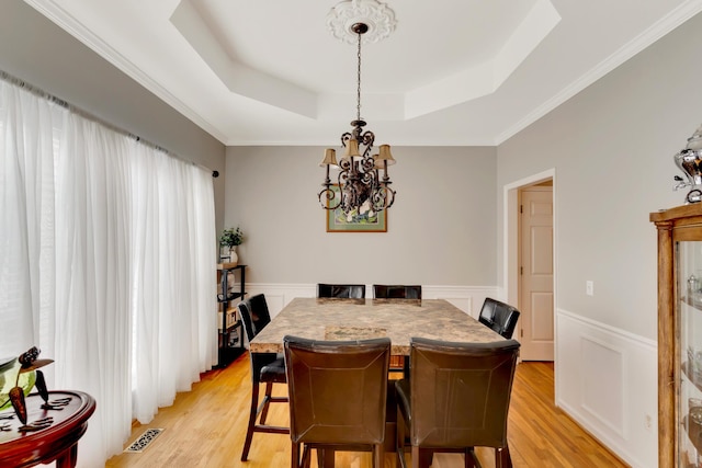 dining room featuring a chandelier, crown molding, a raised ceiling, and light hardwood / wood-style flooring