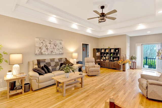 living room with ceiling fan, ornamental molding, a raised ceiling, and light hardwood / wood-style floors