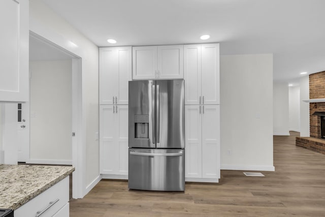 kitchen with light stone counters, a brick fireplace, white cabinetry, and stainless steel fridge