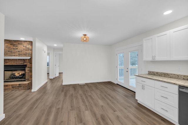 kitchen featuring light stone counters, light wood-type flooring, stainless steel dishwasher, a fireplace, and white cabinets