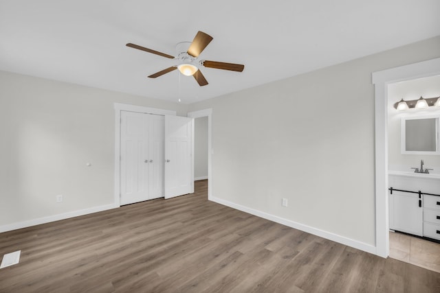 unfurnished bedroom with ensuite bathroom, sink, light wood-type flooring, and a closet