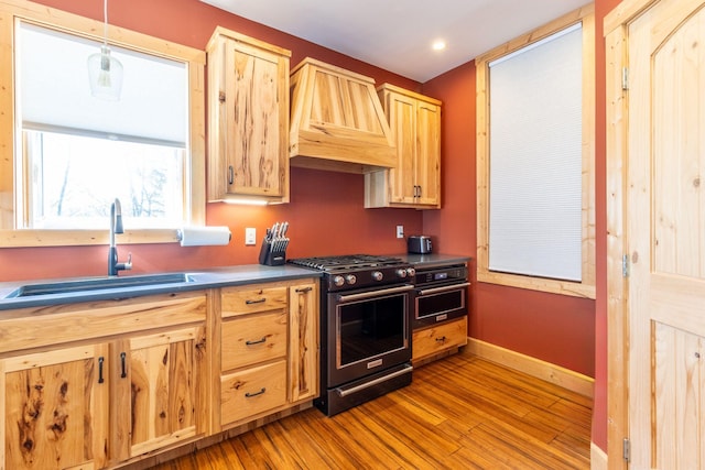 kitchen with premium range hood, stainless steel gas stove, sink, hanging light fixtures, and light brown cabinets