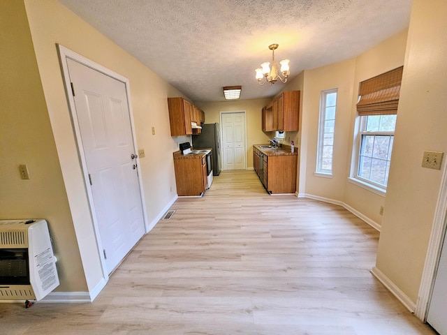 kitchen with heating unit, an inviting chandelier, a textured ceiling, light wood-type flooring, and electric range oven