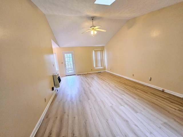 unfurnished living room featuring heating unit, lofted ceiling with skylight, ceiling fan, and light wood-type flooring