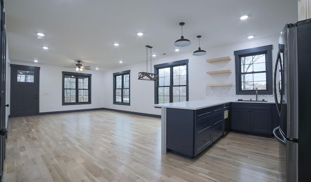 kitchen with sink, light hardwood / wood-style flooring, stainless steel fridge, kitchen peninsula, and decorative backsplash