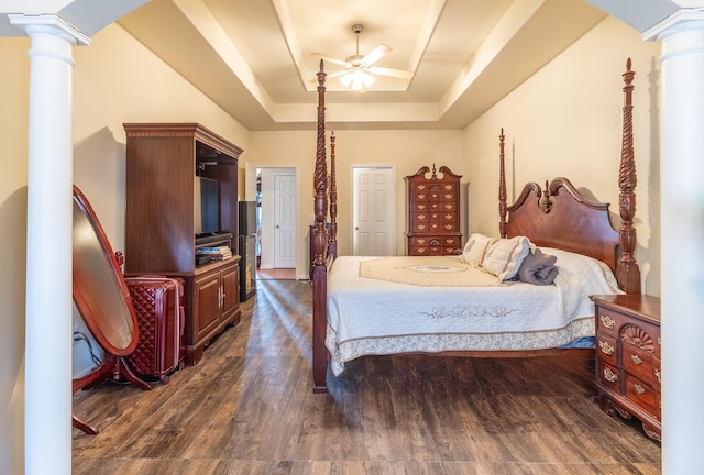 bedroom featuring dark wood-type flooring, decorative columns, a raised ceiling, and ceiling fan