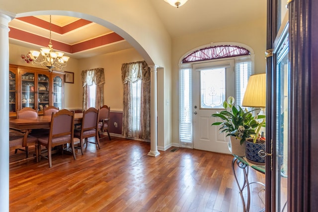 foyer entrance with a tray ceiling, a chandelier, hardwood / wood-style floors, and ornate columns