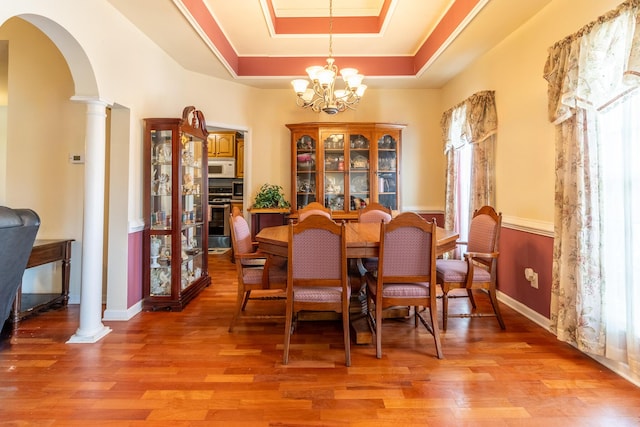 dining space featuring a tray ceiling, a chandelier, light hardwood / wood-style floors, and ornate columns