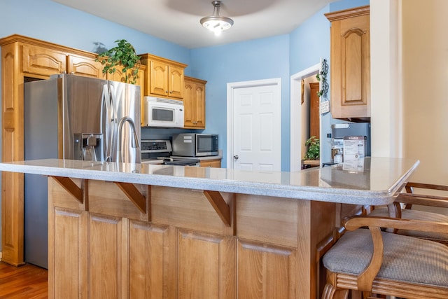 kitchen featuring light hardwood / wood-style floors, appliances with stainless steel finishes, a kitchen bar, and kitchen peninsula