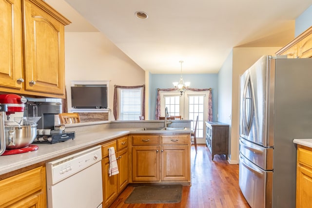 kitchen with sink, hanging light fixtures, stainless steel refrigerator, white dishwasher, and light hardwood / wood-style floors