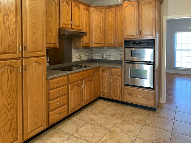 kitchen with tasteful backsplash, black electric stovetop, double oven, and light tile patterned floors