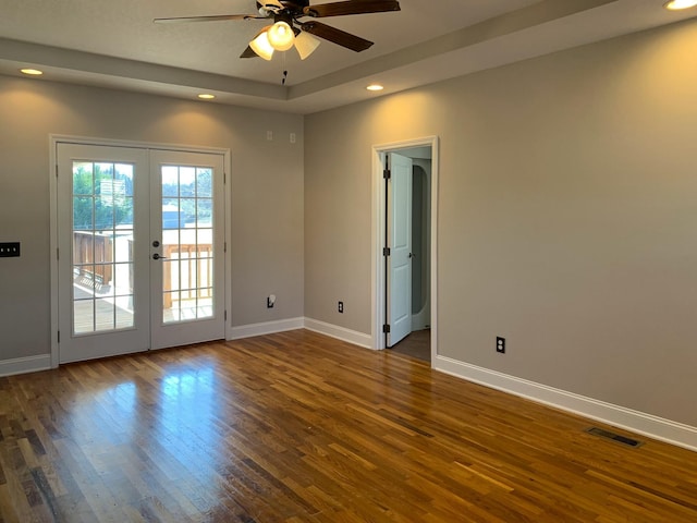 unfurnished room with a tray ceiling, dark wood-type flooring, ceiling fan, and french doors